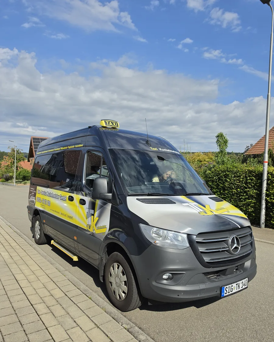 Grauer Mercedes Sprinter mit gelber Beschriftung und Taxischild, schräg von vorn